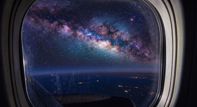 Airplane window view of a star-filled night sky above a dark ocean horizon.