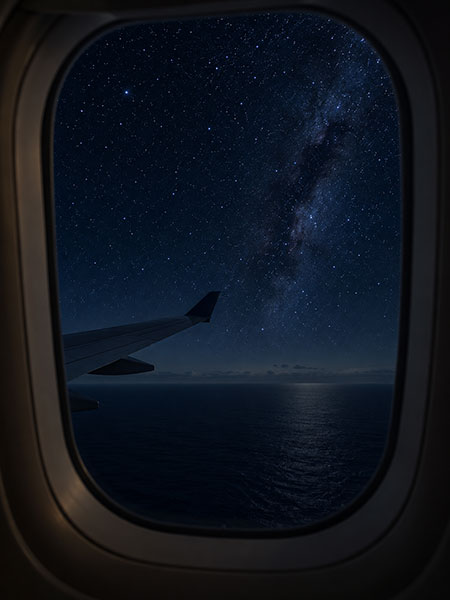 Passenger photographs the Milky Way core through a darkened high-altitude cabin window.